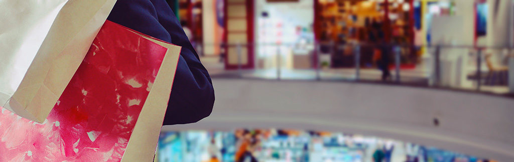 mulher segurando sacolas olhando para lojas em shopping